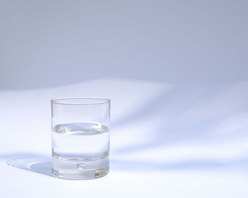 Clear glass of water on a white surface with a soft blue shadow