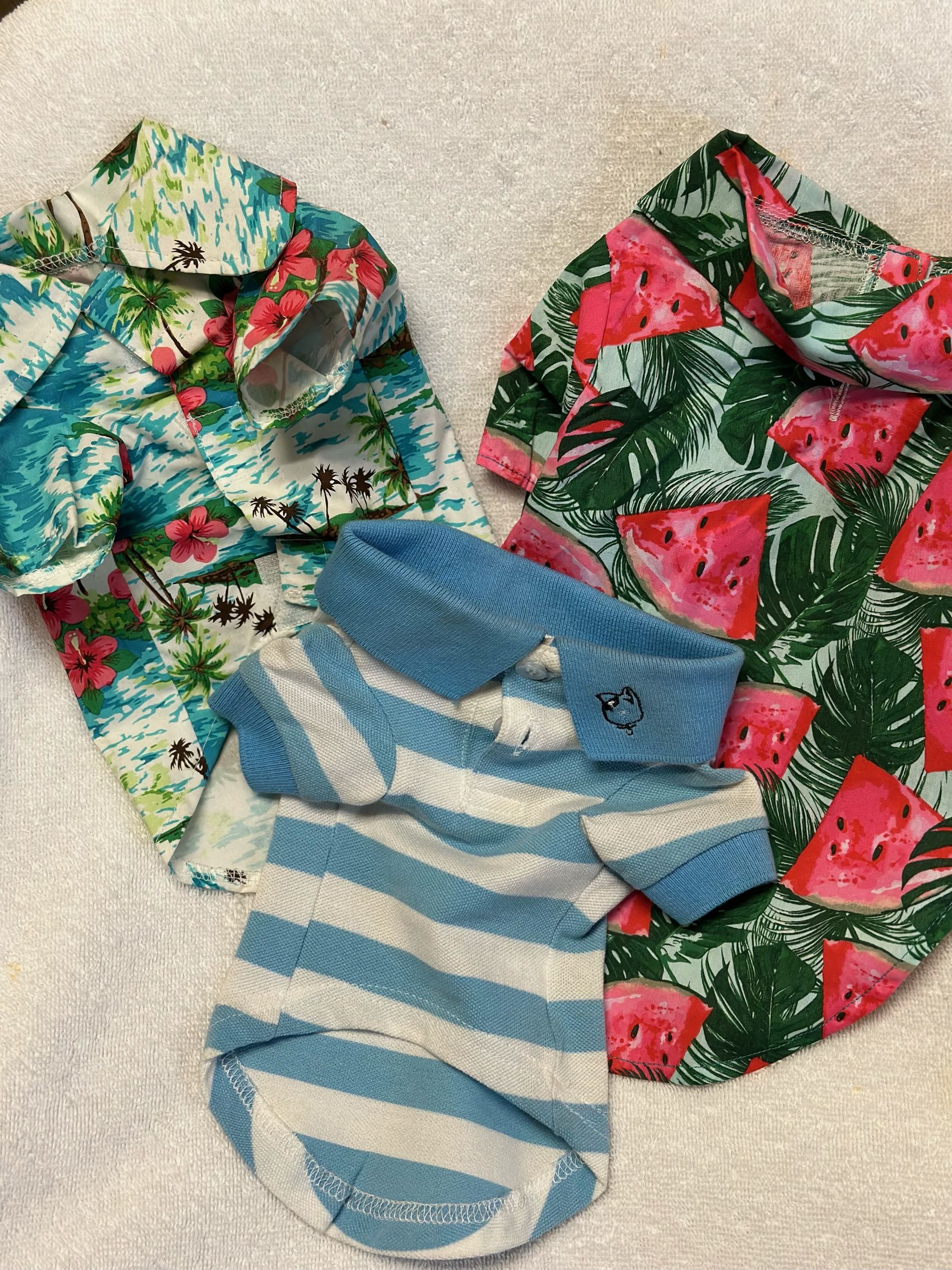 Three shirts with watermelons on them are sitting on a white towel.