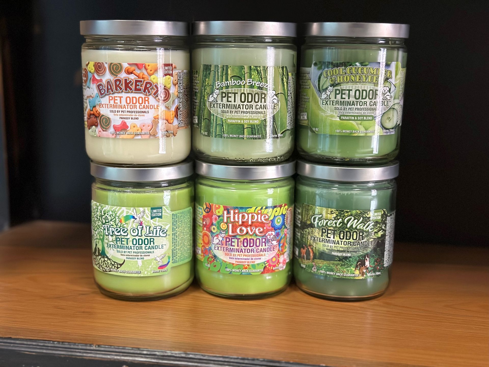 Six jars of candles are stacked on top of each other on a wooden shelf.