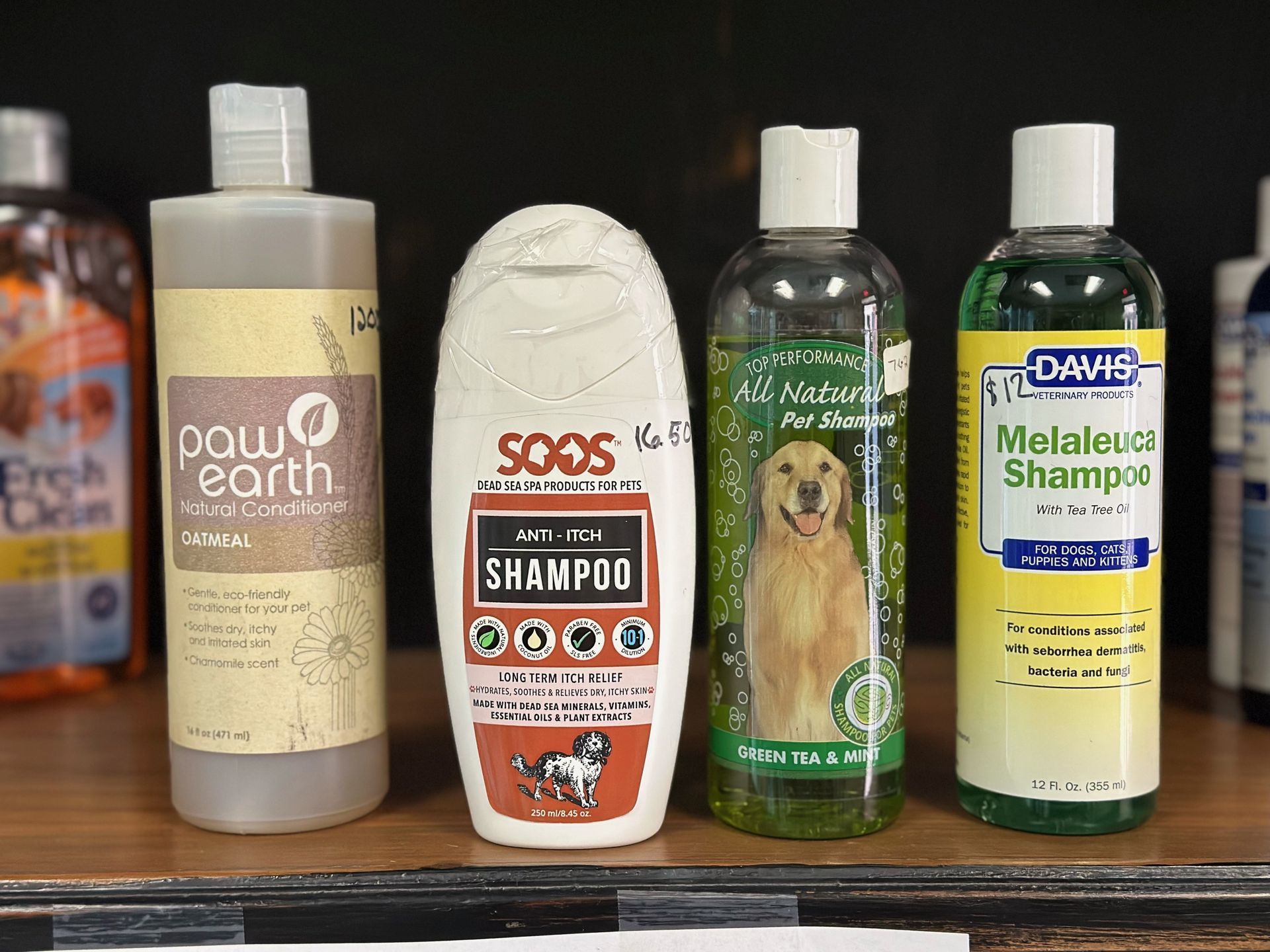 Four bottles of dog shampoo are sitting on a wooden shelf.