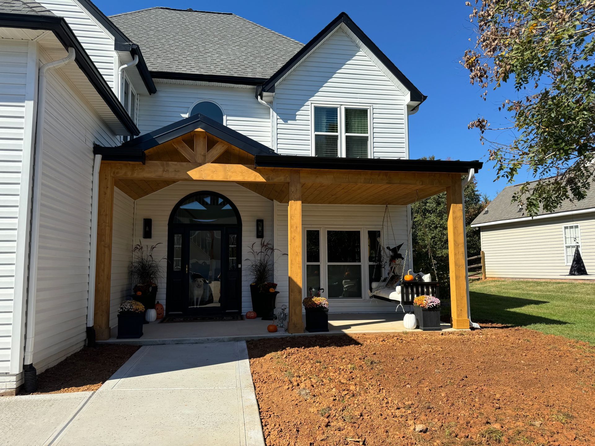 Front entrance of a white house with a covered porch, black door, and landscaped front yard.