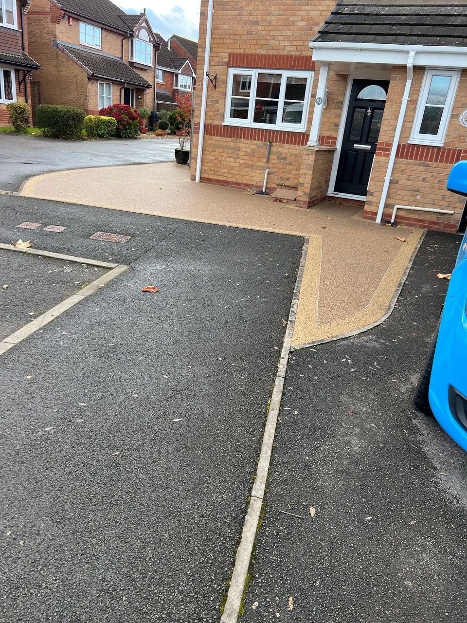 A 10-year-old resin driveway installation in a brown colour, with a purple flower bed on the right-hand side of the driveway.