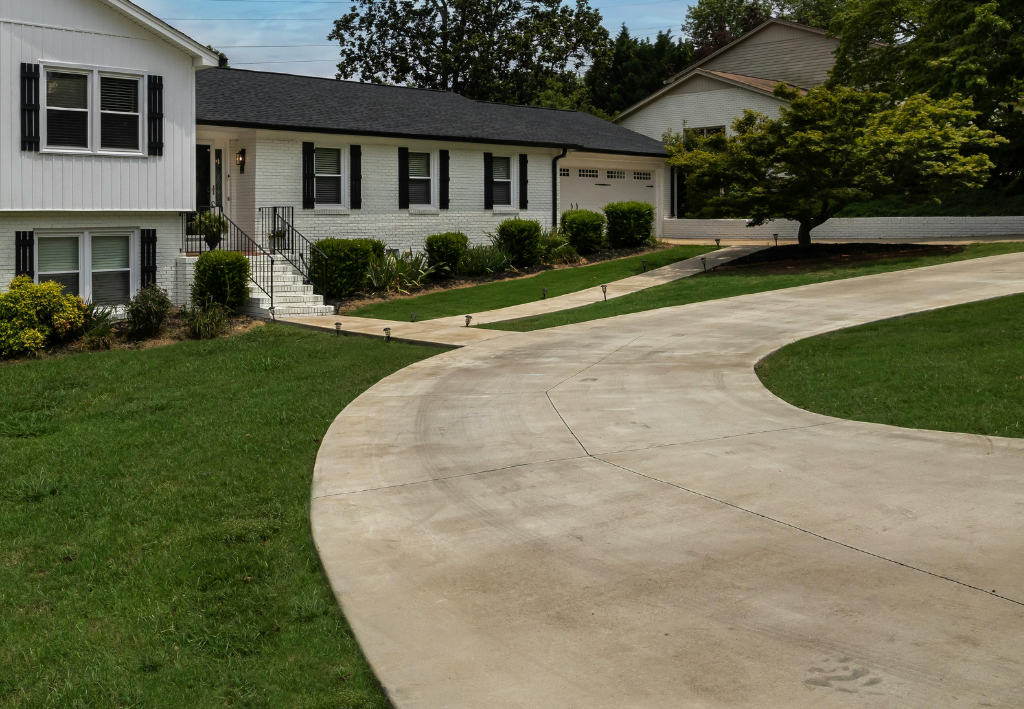 White house with black shutters, driveway, green lawn, and trees.