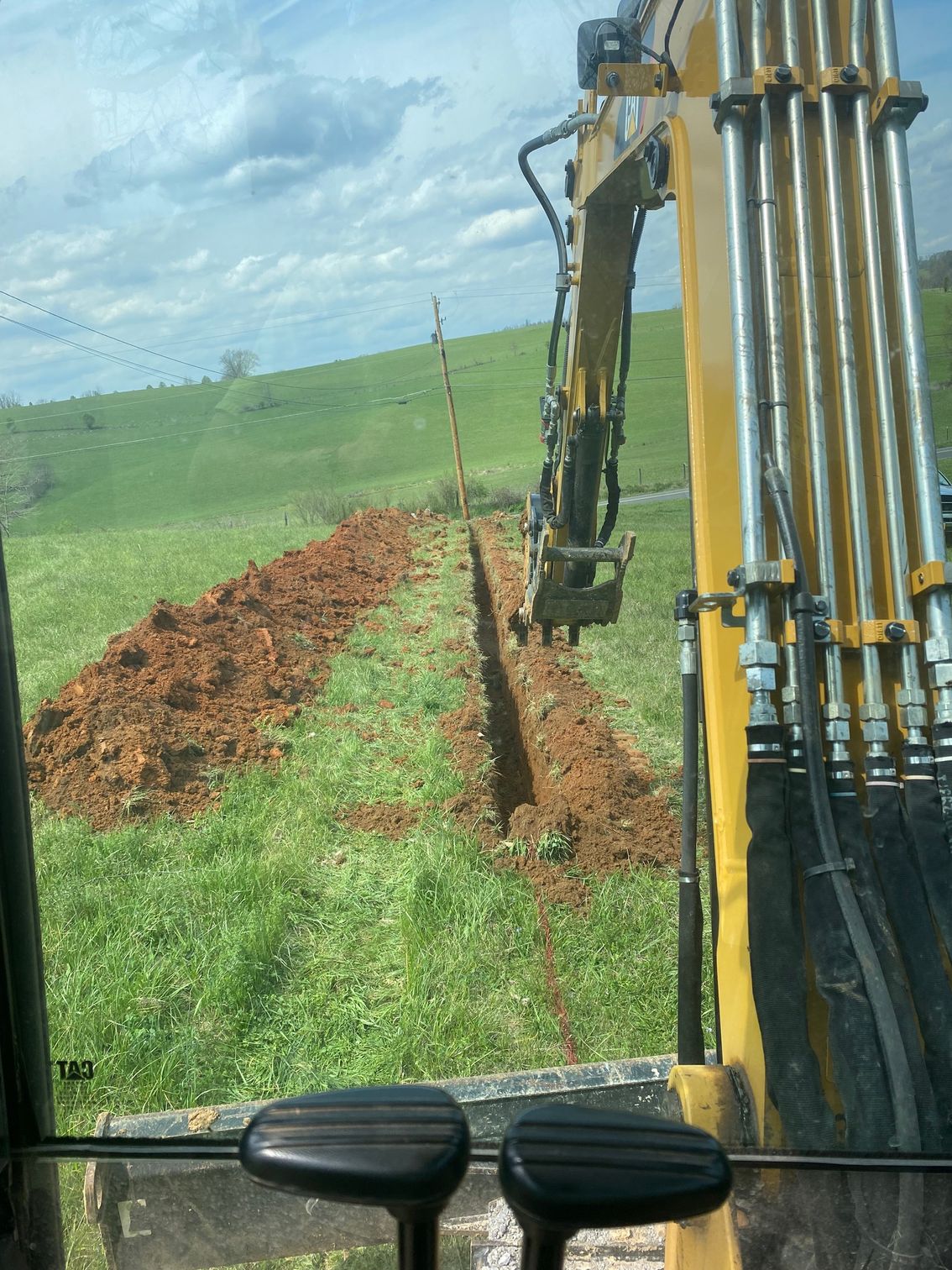 GET A QUOTE! A yellow excavator is digging a trench in a grassy field.