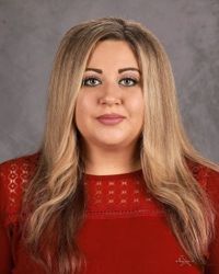 Portrait of a person with long blonde hair in a red top against a gray studio backdrop