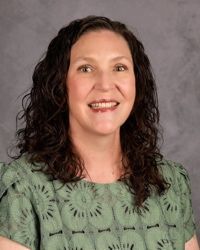 Woman smiling in a green patterned top against a gray studio backdrop