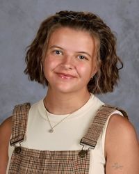 Smiling person in a plaid jumper and cream top against a gray studio backdrop