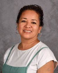 Portrait of a smiling person in a white shirt and green apron against a gray backdrop