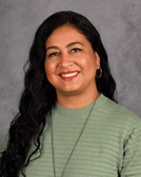 Smiling person with long dark hair wearing a light green ribbed top against a gray backdrop