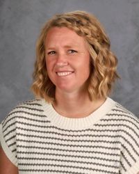Smiling person with wavy blonde hair wearing a black-and-white striped sweater against a gray background