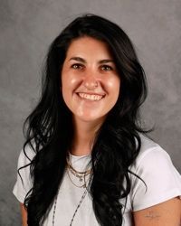 Smiling woman with long dark hair in a white shirt against a gray studio background