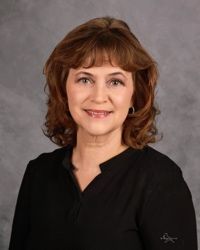 Portrait of a smiling woman in a black top against a gray studio backdrop