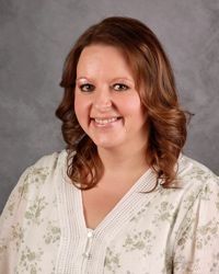 Smiling woman with shoulder-length brown hair wearing a light floral blouse against a gray backdrop