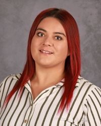 Portrait of a person with red hair in a white striped shirt against a gray studio backdrop