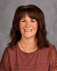 Smiling woman with dark brown hair in a maroon top against a gray studio backdrop