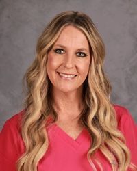 Smiling woman with long blonde hair wearing a bright pink top against a gray background
