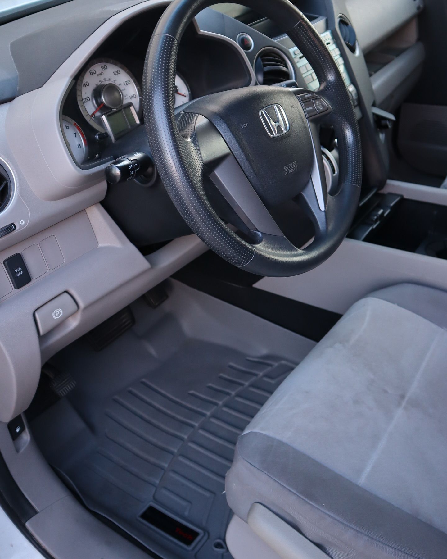 Interior view of a Honda car's front seat, steering wheel, dashboard, and floor mats in gray and black.