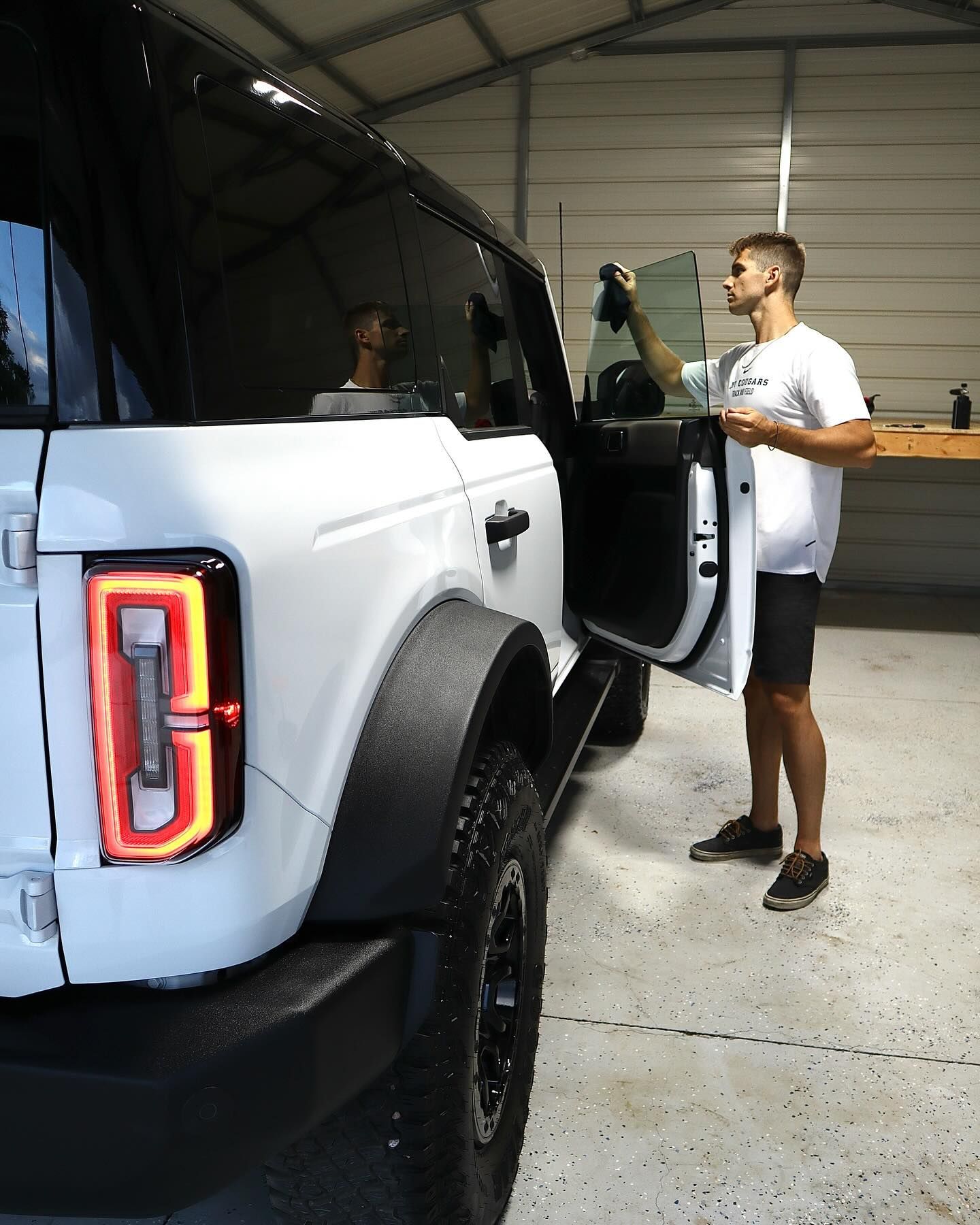 Person applying tint to a white Bronco's window in a garage.