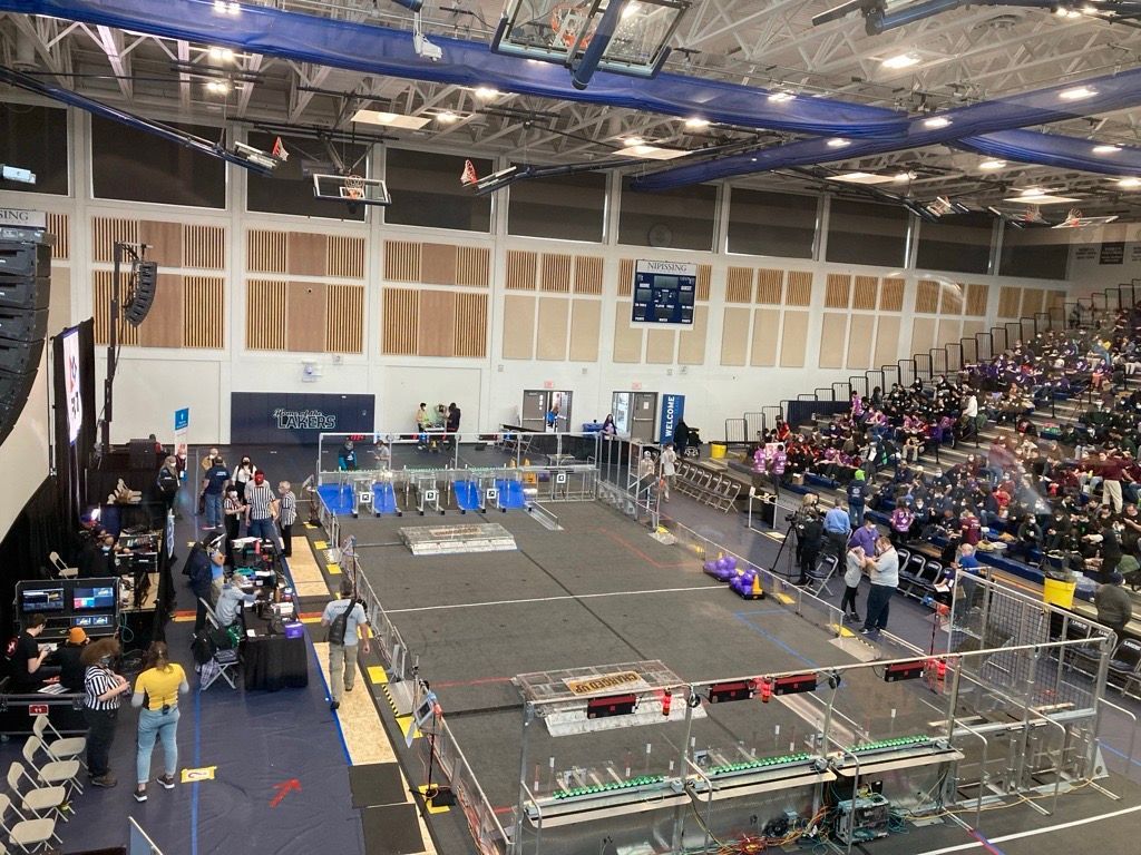 Robotics competition: arena with robots, teams, and audience in a large venue.