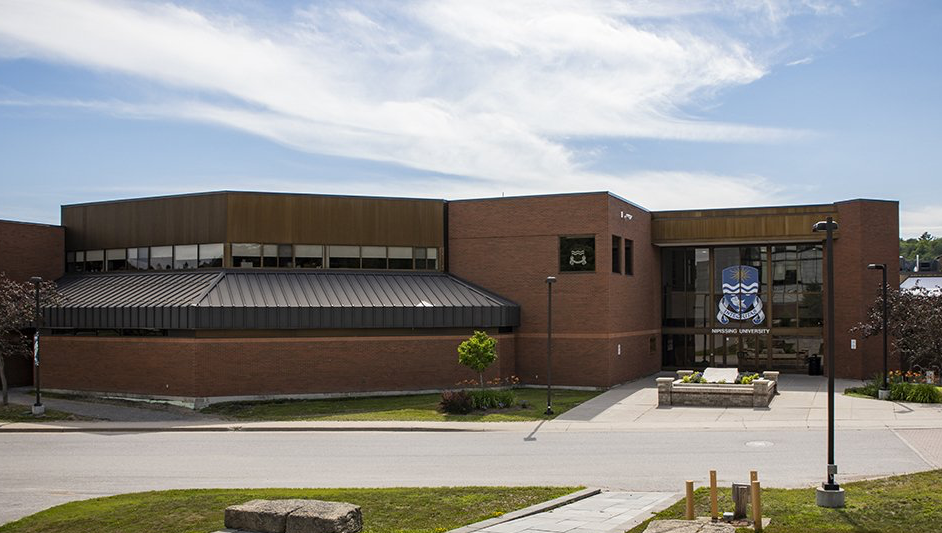A large brick building with a metal roof is sitting on top of a lush green field.