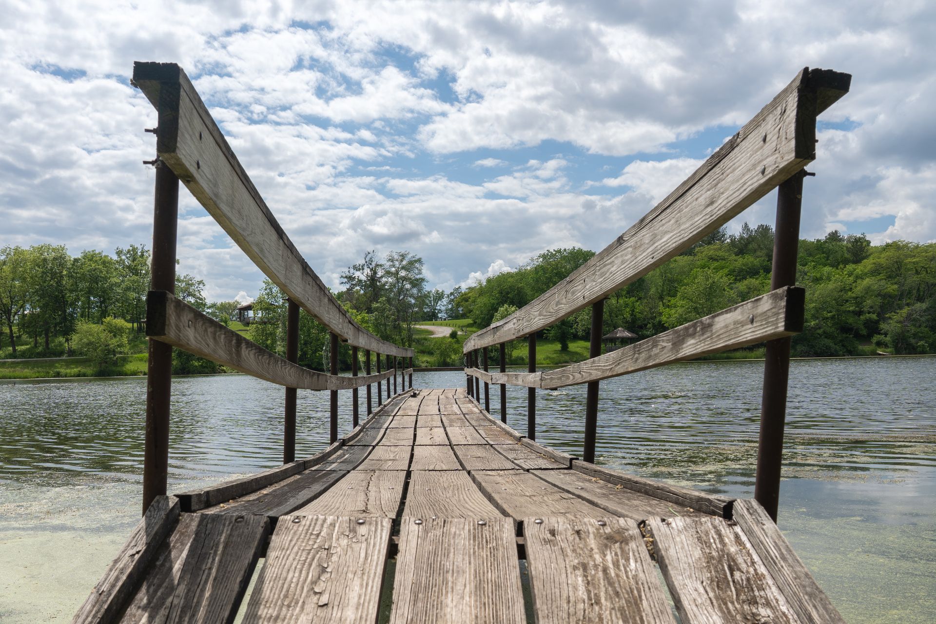 Wooden fishing dock leading to grassy hill surrounded by trees at East Lake Park in Osceola, Iowa