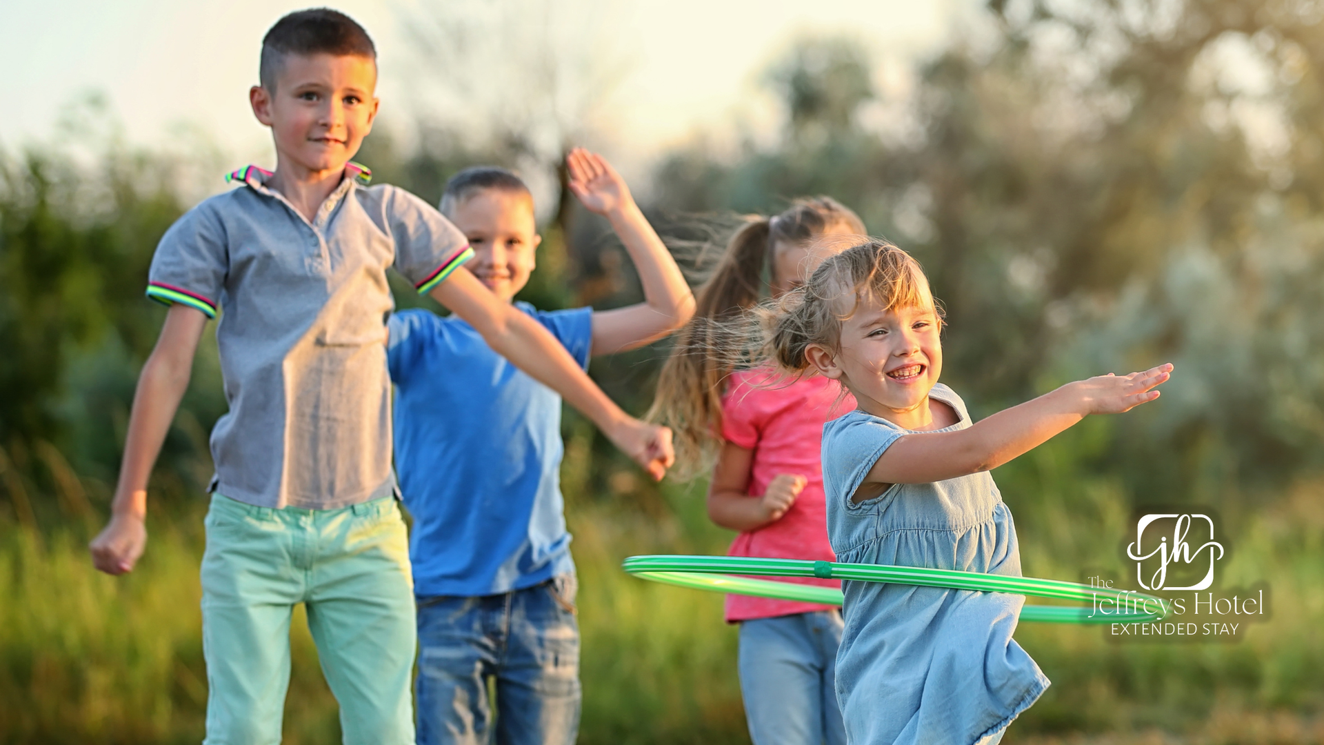 Four children playing outdoors; one girl twirling a green hula hoop, others smiling and waving.