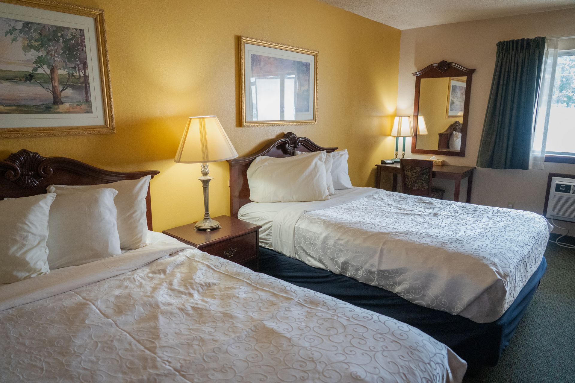 Hotel room with two double beds, nightstand with lamp, and a desk.
