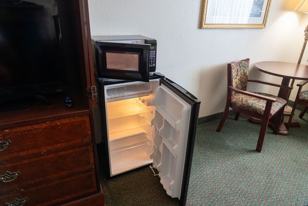 Mini-fridge with open door, microwave on top, and wooden furniture in a room with green carpet.