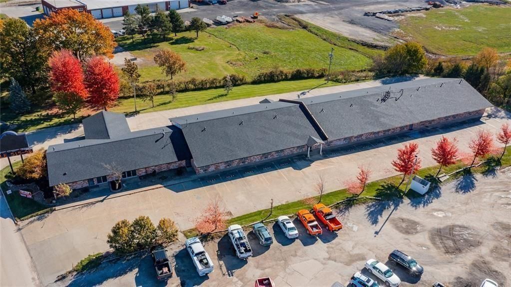 Aerial view of a long, dark-roofed building with cars parked in front, fall foliage.