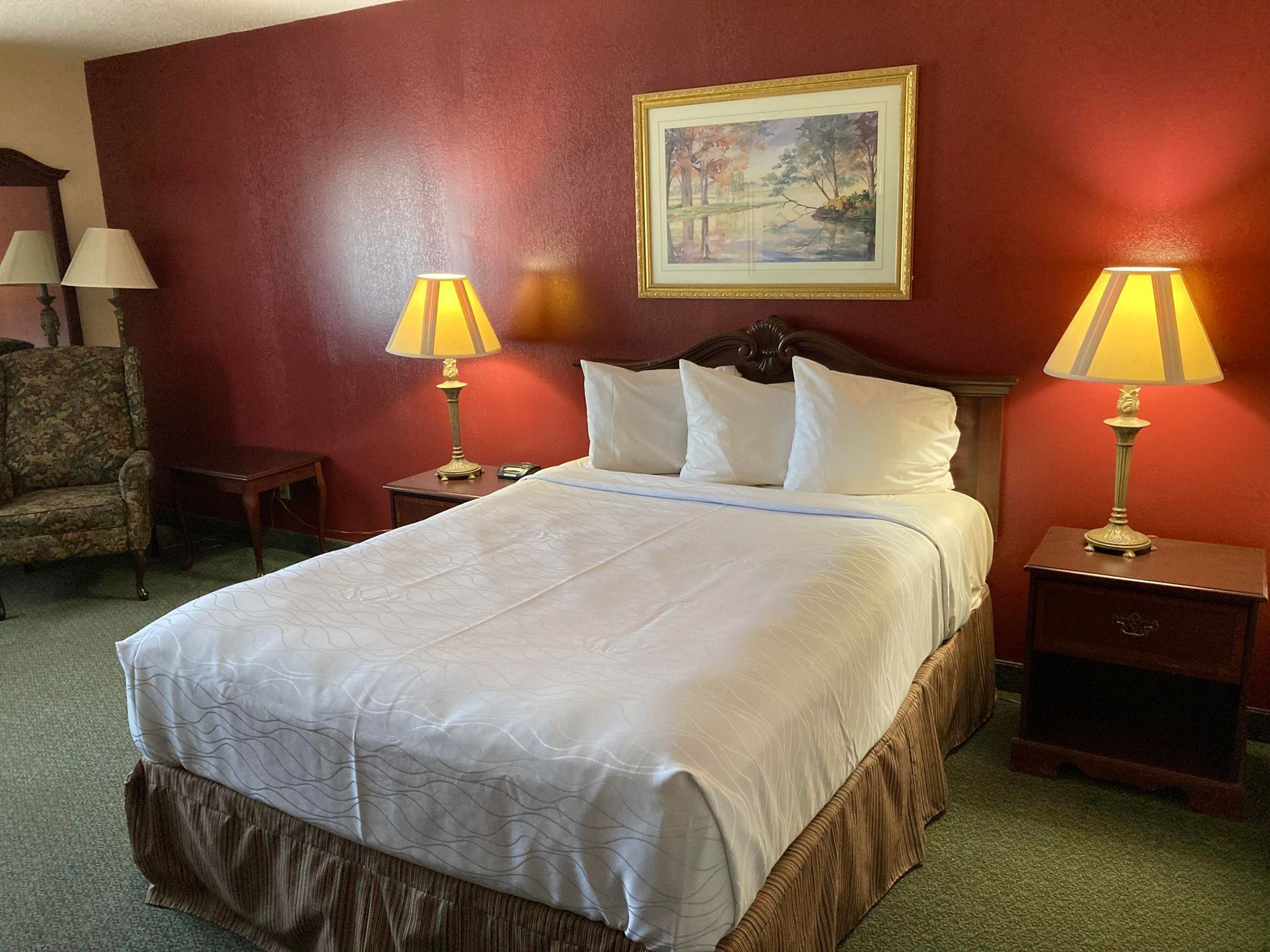 Queen bed guest room with deep red accent wall, artwork, and relaxed seating—ideal for solo or couple stays.