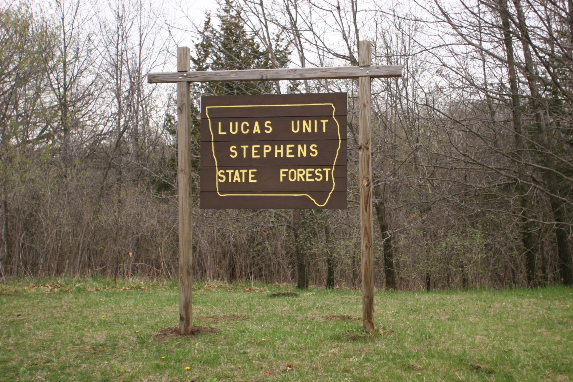 Sign for Lucas Unit Stephens State Forest. Brown wooden sign with lettering, outline of Iowa, set in a grassy area with trees.