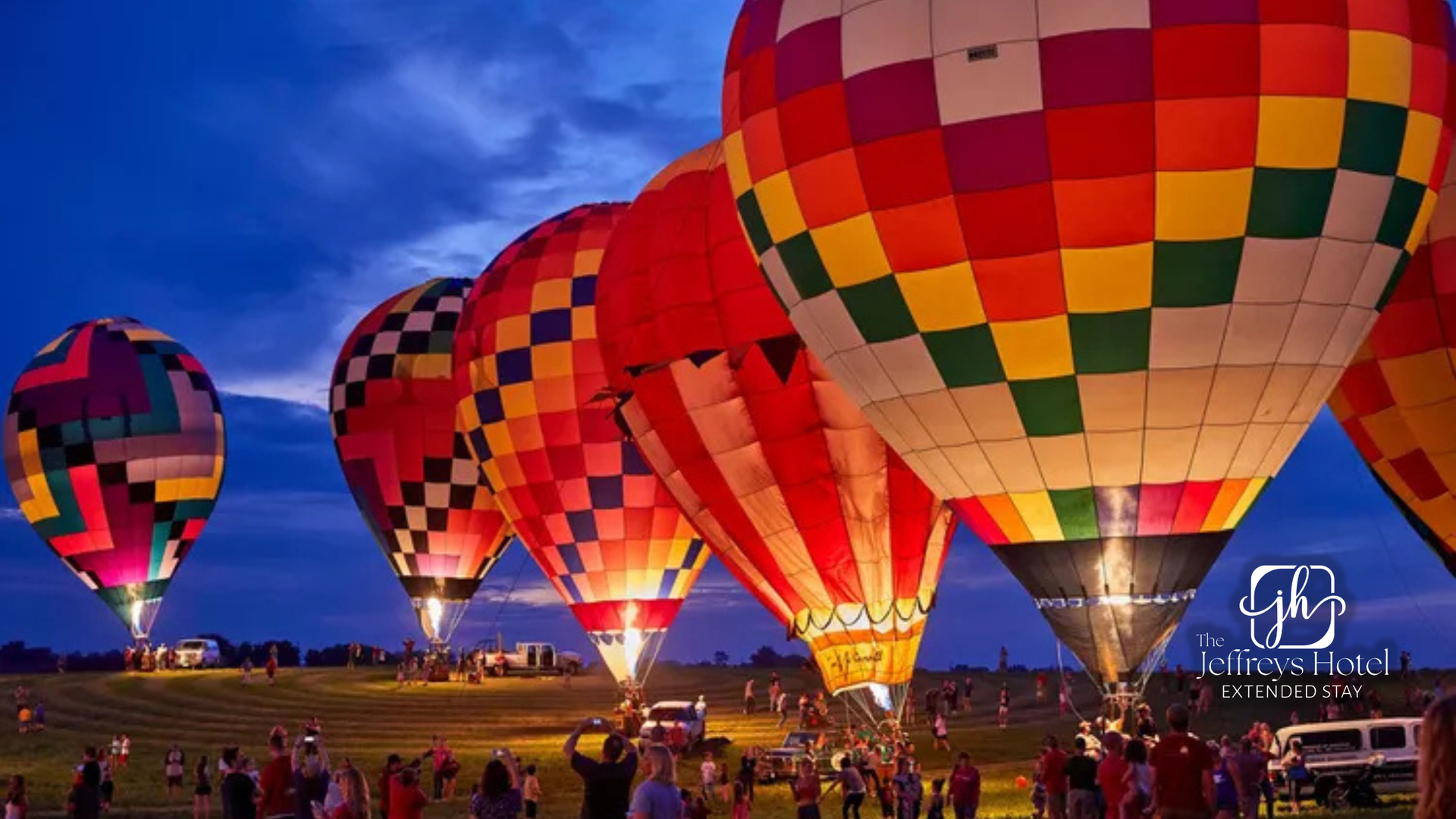 Colorful hot air balloons glowing at dusk, ready for launch, with a crowd watching.