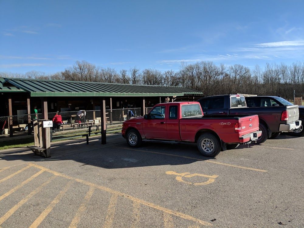Red pickup truck parked near a covered outdoor structure and other vehicles on a sunny day.