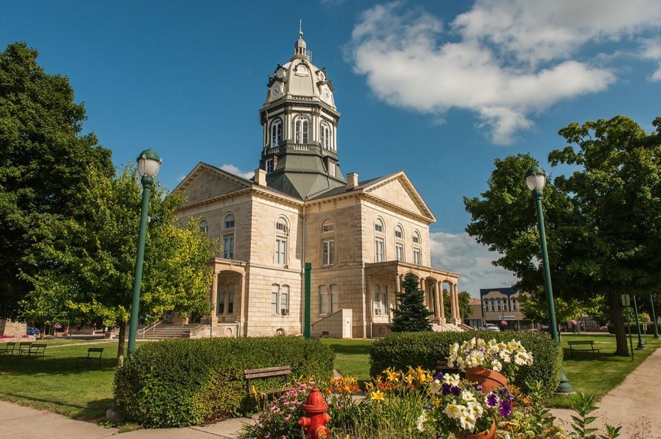 Winterset courthouse with dome, flower beds in front, trees, and blue sky.