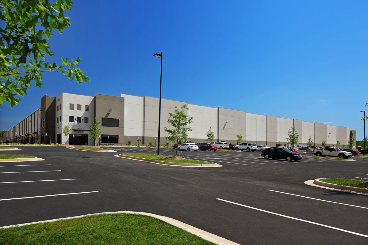 Large warehouse building with parking lot and cars on a sunny day.