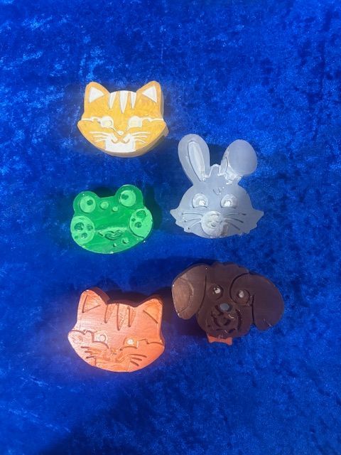 Five small animal face charms in yellow cat, green frog, gray bunny, peach cat, and brown dog on blue fabric