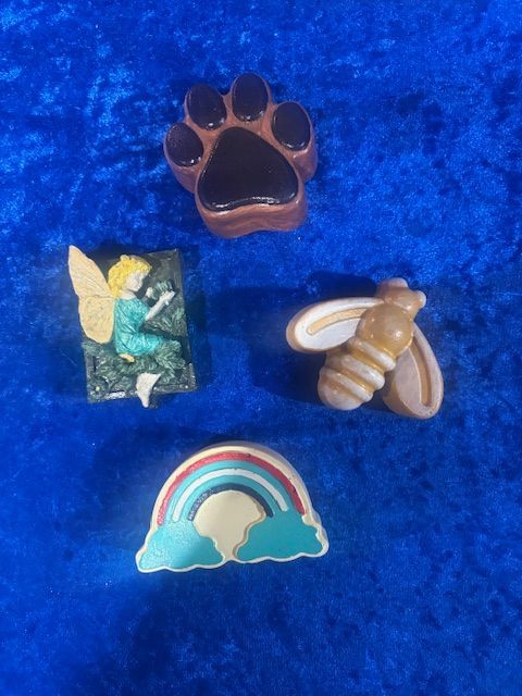 Assorted small pins on blue velvet: paw print, fairy, bee, and rainbow cloud.
