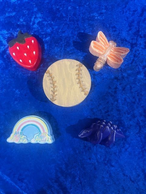 Small colorful toy charms on blue fabric: strawberry, baseball, butterfly, rainbow, and purple leaves