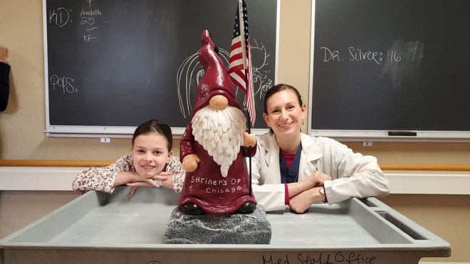Girl and woman smiling beside a red gnome statue in a classroom