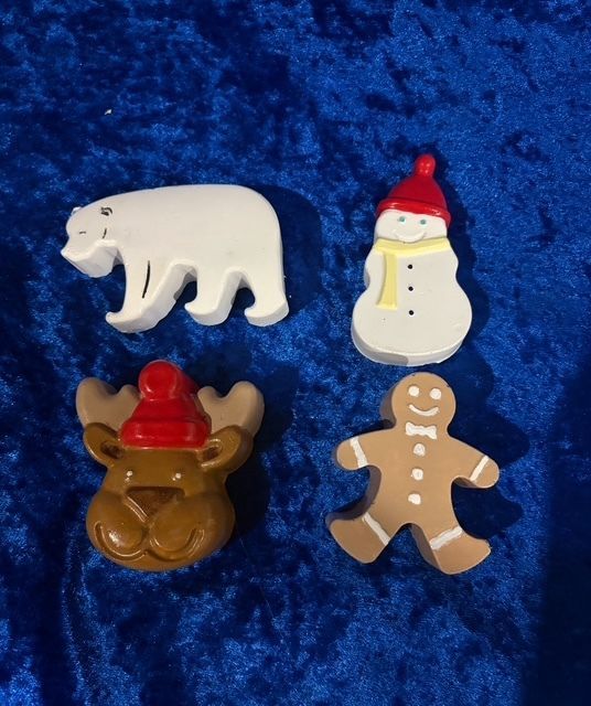 Four holiday-shaped magnets: polar bear, snowman, reindeer, and gingerbread man on blue fabric.