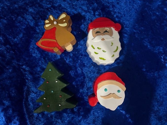 Four Christmas cookie ornaments: bell, Santa, tree, and snowman on blue background