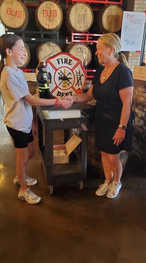 Two women standing by a fire department emblem in a barrel-lined indoor space