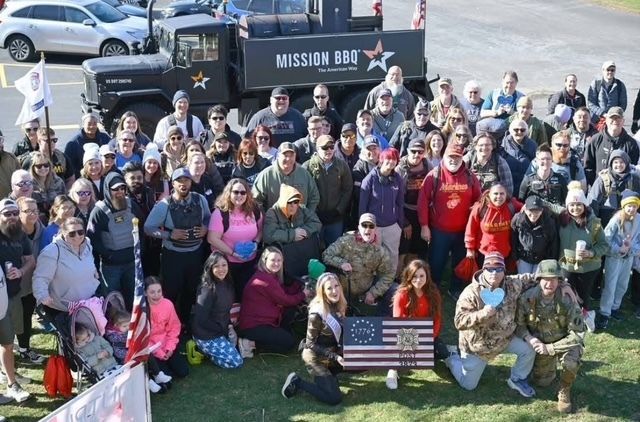 Large group posing outdoors with an American flag banner and a Mississippi 88X truck in the background.