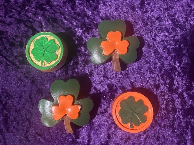 Four clover-shaped flower pins in green, orange, and black on purple fabric.