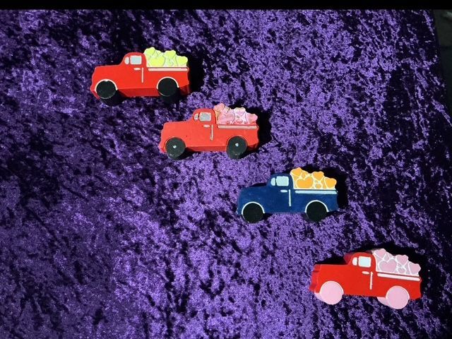 Four toy trucks in red, orange, blue, and red on a purple textured background.