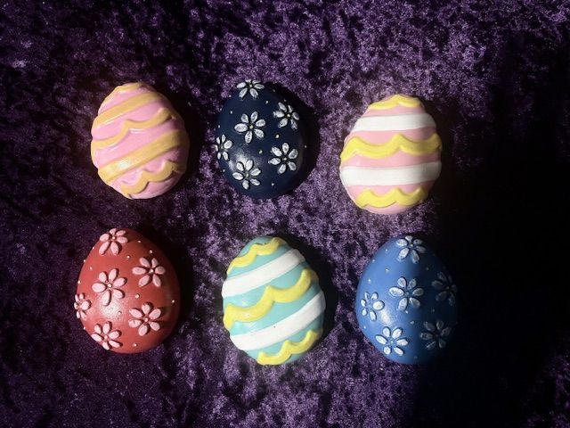 Six decorated Easter eggs on a purple fuzzy background.