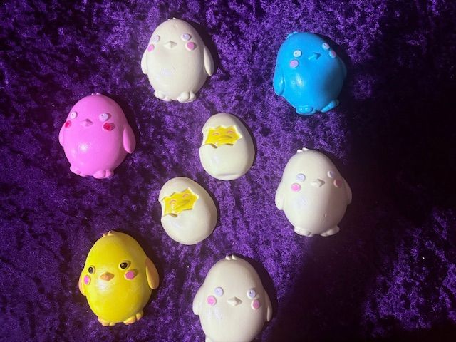 Small pastel bird figurines on purple fabric, including pink, white, blue, and yellow ones.