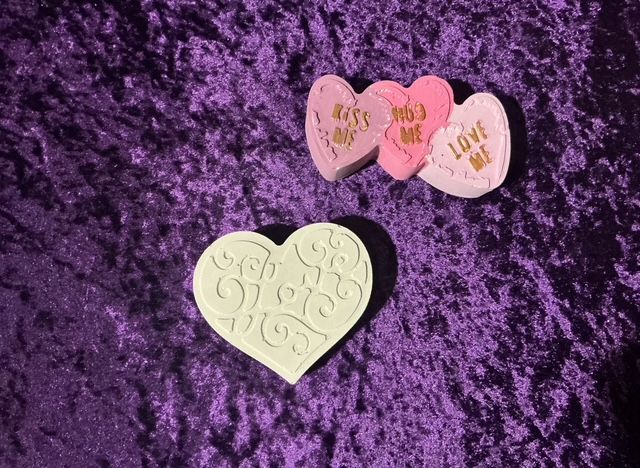 Three heart-shaped candies on purple fabric, with a larger cream heart in front.