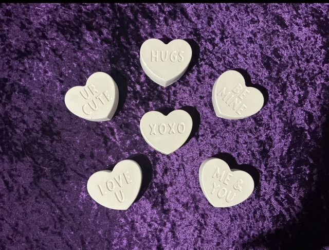 Five candy hearts on purple fur, reading HUGS, XOXO, LOVE and other Valentine messages