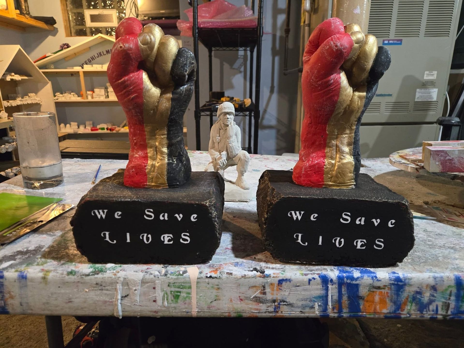 Two painted sculptures on a worktable, each on a black base reading “we save lives.”